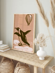 Illustrative penguin and hot air balloon art print on a warm beige background, in an alternate framed mockup