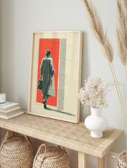 Figure in long coat walking into red background with halftone texture and cream border, in an alternate framed mockup