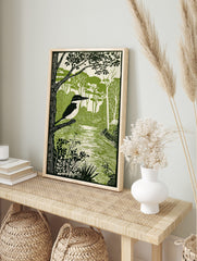Illustrative green and white print of a pied kingfisher on a branch by a river with dense, in an alternate framed mockup