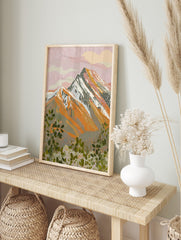 Illustrative mountain landscape print with pink sky, orange peaks, and green foliage, in an alternate framed mockup