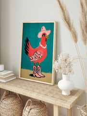 Pink chicken illustration wearing a cowboy hat, pearl necklace, and pink cowboy boots on a, in an alternate framed mockup