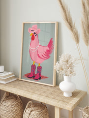Illustrative pink chicken wearing a cowboy hat, pearl necklace, and pink cowboy boots on a, in an alternate framed mockup