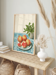 Illustrative pomegranate wall art with whole and sliced pomegranates on a plate, blue tablecloth, and green plant. - Image 3