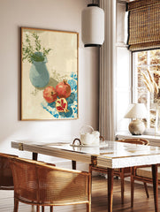 Pomegranate wall art with two red pomegranates, one cut, on a blue patterned cloth next to a blue vase with green leaves. - Image 2