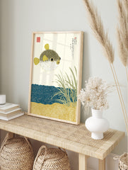 Illustrative pufferfish print with Japanese text, sea grass, and patterned blue water and sand, in an alternate framed mockup