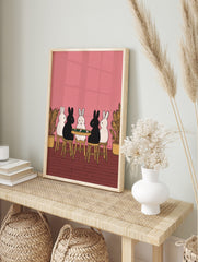 Illustrative print of five black and white rabbits playing cards at a green table on a pink, in an alternate framed mockup