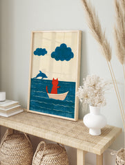Illustration of a red cat sitting in a white boat on a blue sea with a jumping dolphin and, in an alternate framed mockup