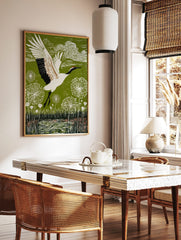 Red-crowned crane in flight over green landscape with white dandelion seed heads and water, in a styled room mockup