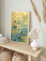 Illustrative print of red-crowned cranes wading in blue water amongst golden reeds with, in an alternate framed mockup