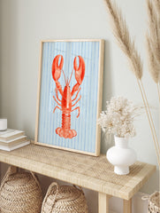 Illustrative red lobster wall art print on a light blue background with vertical blue stripes, in an alternate framed mockup