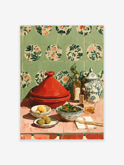 Red tagine pot, lemons, olives, salad, oil bottles, and patterned jar on pink table with green floral tiled wall