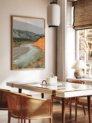 Illustrative landscape art print with a winding river, orange hill, and grey mountains under a, in a styled room mockup