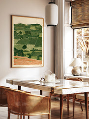 Rolling hills landscape wall art with layered green fields and orange foreground in an illustrative, in a styled room mockup