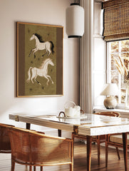 Illustrative art print of two running horses in off-white on an olive green background with black, in a styled room mockup