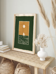 Minimalist sailboat wall art illustration with a green sea, tan sky, and white sun, in a, in an alternate framed mockup