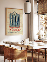 Vintage-style illustration of three blue sardines in a tin can with red 'SARDINES DE LA MÈR' text, in a styled room mockup