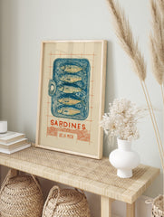 Illustrative linocut-style print of a blue sardine tin with five fish, 'Sardines Dé La Mer', in an alternate framed mockup