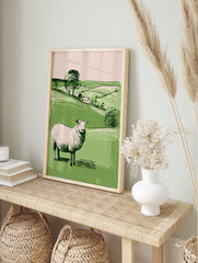 Illustrative white sheep in green pastoral landscape with hills, trees, and two cottages, in an alternate framed mockup