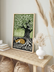 Woodcut style print of a sleeping russet fox curled at the base of a large tree with green, in an alternate framed mockup