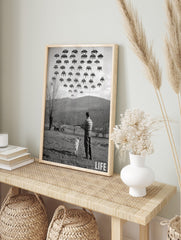 Monochrome print of a man and dog aiming shotgun at pixelated Space Invaders in a rural, in an alternate framed mockup