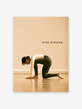 Woman in kneeling yoga pose on wooden floor with STAY STRONG text on beige background