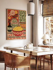 Still life folk art print with a bowl of pasta, flowers in vases, and patterned textiles on a red, in a styled room mockup