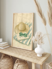 Illustrative print of a straw hat, round green sunglasses, and a notebook on a blue and white, in an alternate framed mockup