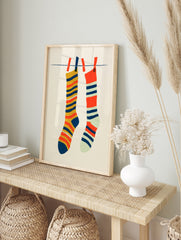 Illustrative art print of two striped socks hanging on a laundry line against a cream, in an alternate framed mockup