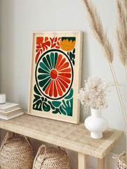 Abstract floral wheel art print with radiating orange and teal segments, surrounded by green, in an alternate framed mockup
