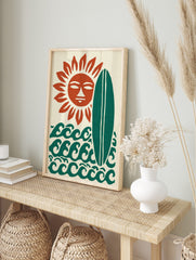Stylised sun with a face, green surfboard, and ocean waves on a cream background art print, in an alternate framed mockup