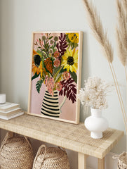 Illustrative sunflower and pink floral bouquet in a striped jug on a pink background, in an alternate framed mockup