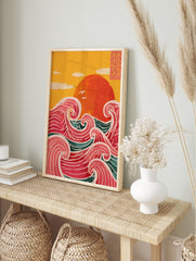 Illustrative print of a large red sun over stylised pink and teal ocean waves with a yellow, in an alternate framed mockup
