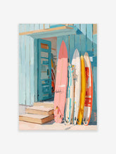 Colourful surfboards in pink, yellow, and white leaning against a blue wooden beach shack with an open door