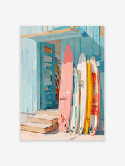 Colourful surfboards in pink, yellow, and white leaning against a blue wooden beach shack with an open door