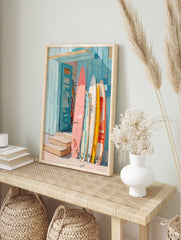 Colourful surfboards in pink, yellow, and white leaning against a blue wooden beach shack, in an alternate framed mockup