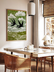 Stylised linocut print of two black swallows flying over green fields and white clouds in a green, in a styled room mockup