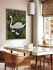 White swan and two cygnets swimming in dark water, surrounded by green reeds and white flowers, in, in a styled room mockup