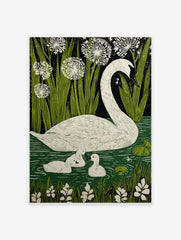 White swan and two cygnets swimming in green water with reeds and white flowers against a dark background