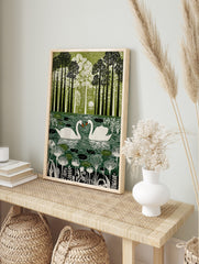 Illustrative green wall art print of two white swans on a pond surrounded by tall trees and, in an alternate framed mockup