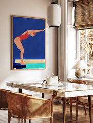 Illustrative wall art of a swimmer in a red swimsuit and cap, poised on a starting block above turquoise water, against a blue background, displayed as the same artwork in a styled poster mockup for home decor