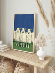Illustrative art print of three white sheep standing in a green field against a solid deep, in an alternate framed mockup