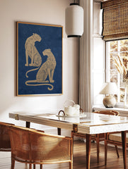Two golden illustrative leopards with intricate patterns seated on a navy blue background, portrait, in a styled room mockup