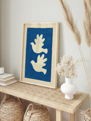 Minimalist art print with two white doves flying left on a solid blue background, in an alternate framed mockup