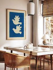 Minimalist art print with two white doves flying left on a solid blue background, in a styled room mockup