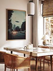 Retro sci-fi print of a UFO flying over a city skyline with cars and buildings at dusk, in a styled room mockup
