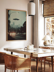 Retro photographic print of a flying saucer hovering over a hazy city street with car headlights, in a styled room mockup