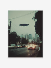 Photographic print of a dark disc-shaped UFO hovering over a city street with cars and buildings at dusk