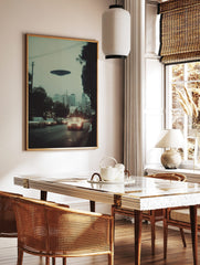 Photographic print of a dark disc-shaped UFO hovering over a city street with cars and buildings at, in a styled room mockup