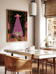 Whimsical illustrative wall art of a black and white cow being abducted by a purple UFO beam in a, in a styled room mockup