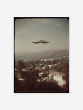 Vintage UFO wall art print showing a classic flying saucer over a hillside town and mountains under a muted sky.
